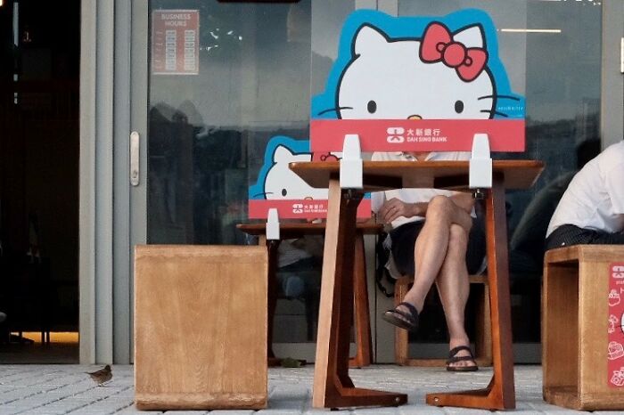 Person sitting behind a table with a Hello Kitty sign perfectly aligned to cover their face in a lucky accident photo.