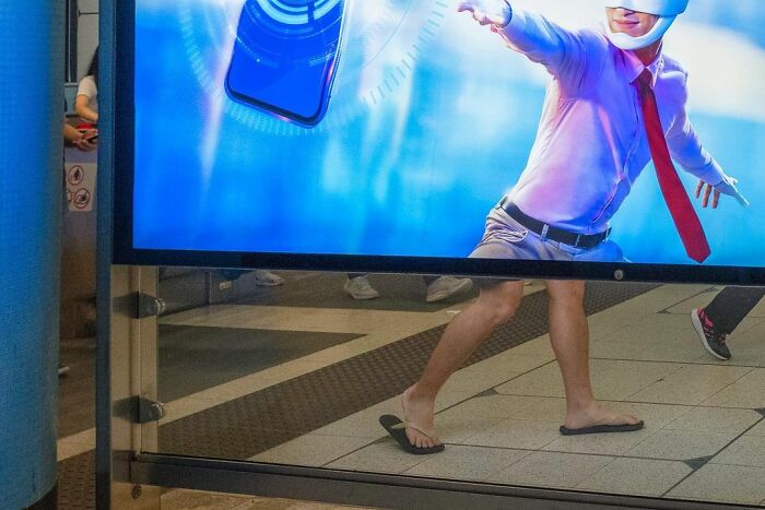 Person walking behind an ad board perfectly aligned to create a lucky accident illusion by photographer Edas Wong.