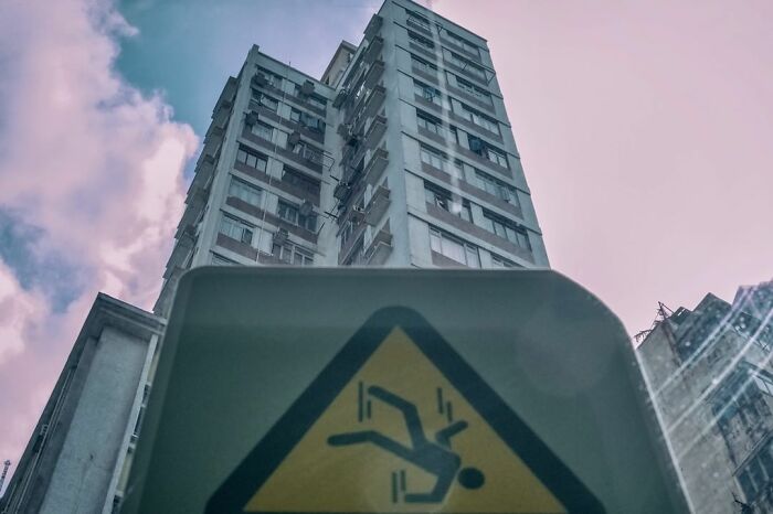 Warning sign showing a person falling in front of a tall building, capturing a lucky accident by photographer Edas Wong.