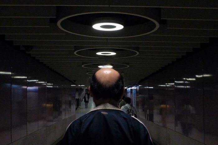 Bald man walking in a dark tunnel with circular lights above, a lucky accident captured by photographer Edas Wong.