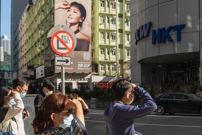 Group of people wearing masks shielding eyes from sun on busy city street, a lucky accident captured by photographer Edas Wong