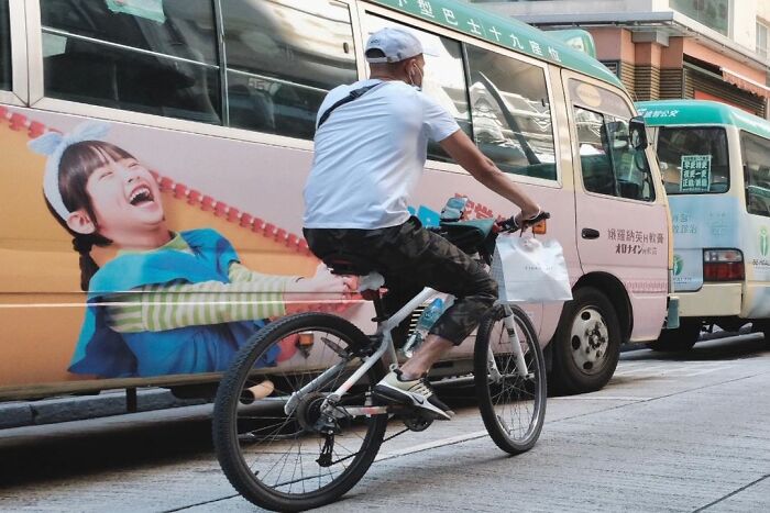 Man on bicycle aligned with bus advertisement, creating a lucky accident captured by photographer Edas Wong on busy street.
