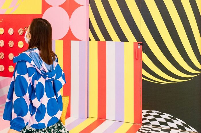 Woman in a blue polka dot jacket walking past bold colorful striped and checkered patterns in lucky accidents captured by Edas Wong.