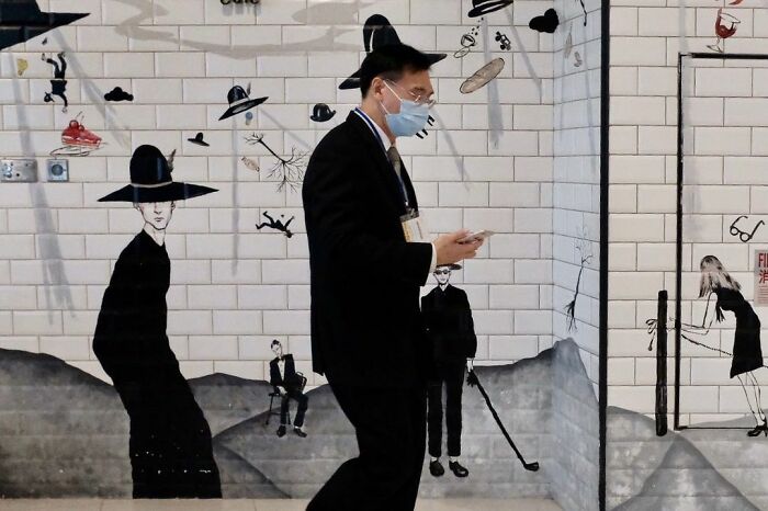 Man wearing mask walking past mural artwork showing people with hats, a golf club, and floating objects, lucky accidents photo.