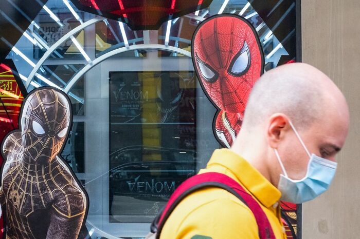 Man wearing a face mask walking past a store window with Spider-Man posters, capturing a lucky accident moment.