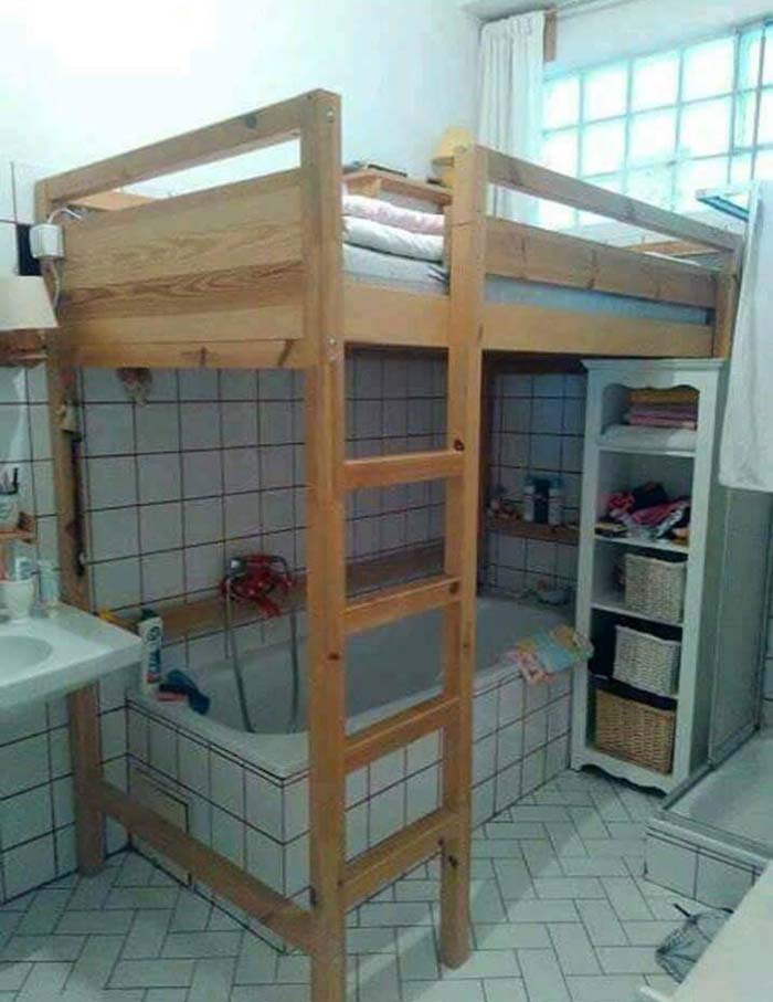 Awful interior with a loft bed awkwardly built over a bathtub in a cramped bathroom space.