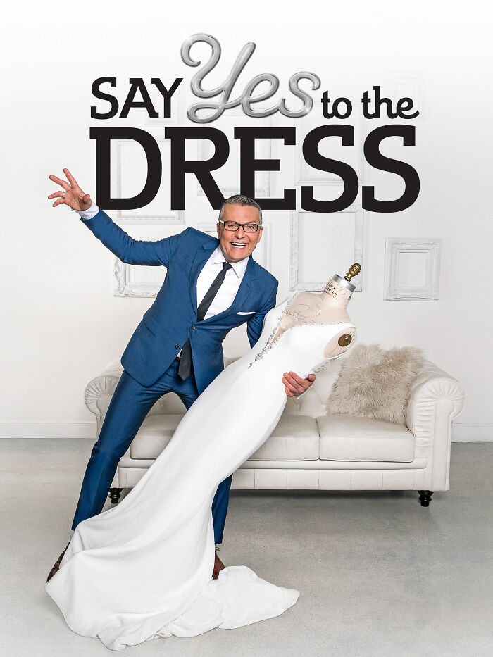 Host in a blue suit posing with a wedding dress on a mannequin, representing reality TV and its fake aspects.