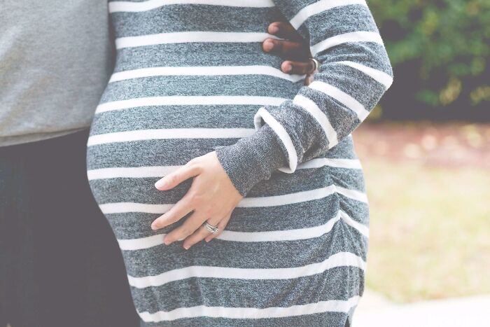 Close-up of a pregnant person wearing a striped shirt with hands gently resting on the belly, illustrating reality TV changes.