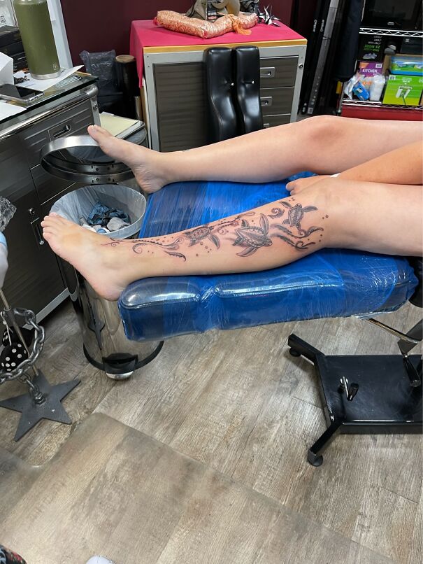 Leg with impressive new tattoo featuring turtles and leaves, resting on a blue covered chair in a tattoo studio.