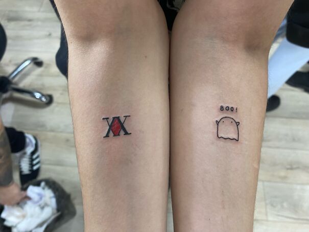 Minimalist tattoos on forearms: a red diamond with 'XX' and a cute ghost saying 'Boo!'.