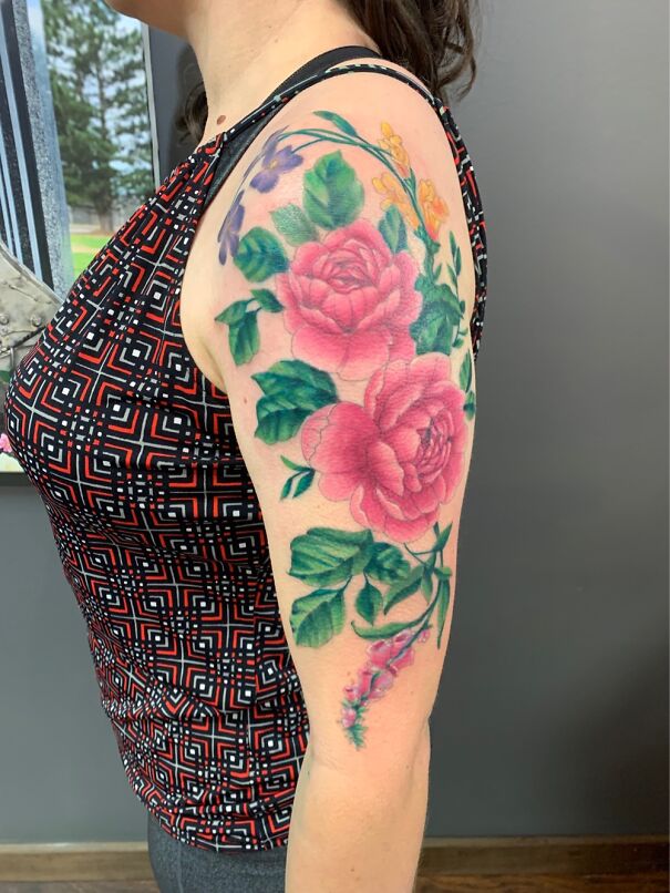 Vibrant floral tattoo on a woman's upper arm, featuring pink roses and green leaves.