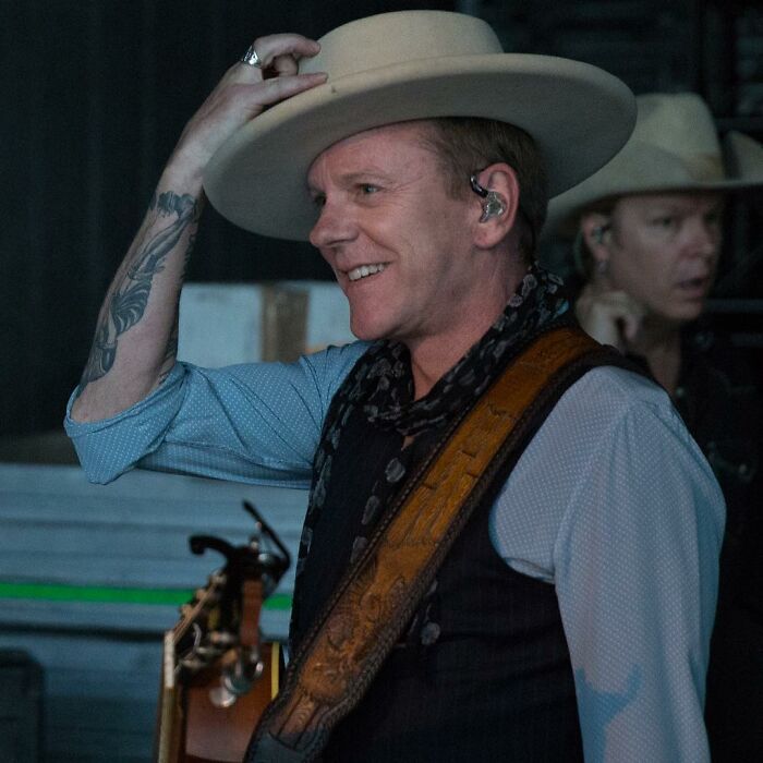 Actor smiling backstage wearing a cowboy hat and guitar strap, representing actors who revive careers with a role.