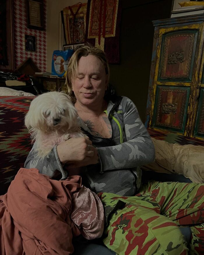 Middle-aged man in casual wear sitting indoors, holding a small white dog, highlighting actors who revived their career.