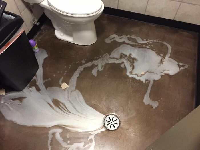 Unusual bathroom interior with a toilet and abstract designs on the floor around a central drain.