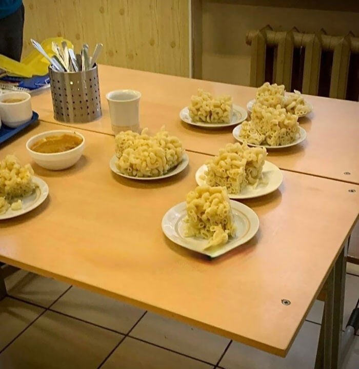 School lunches from around the world showing unusual stacked pasta servings on plates in a cafeteria setting
