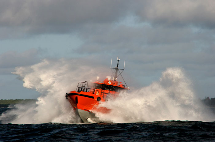 Orange boat cutting through rough sea waves under a cloudy sky, illustrating deep sea diving experiences and underwater challenges.