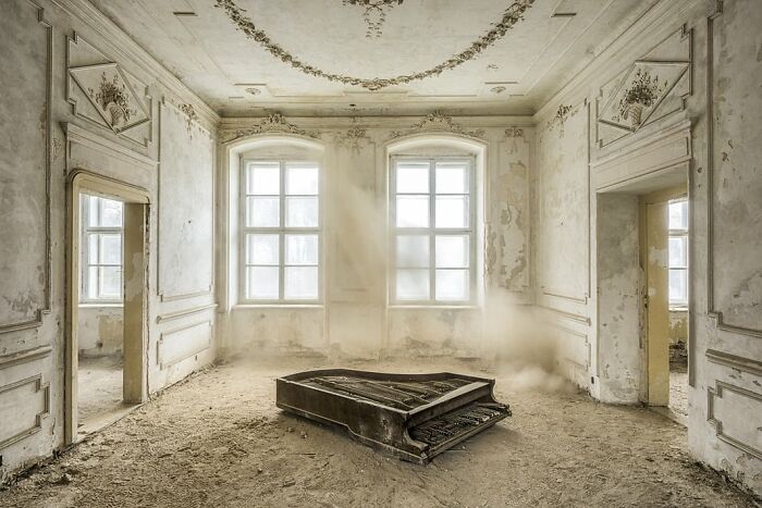 Abandoned grand piano in dusty, decayed room with ornate walls and windows showcasing Budapest International Photo Awards style.