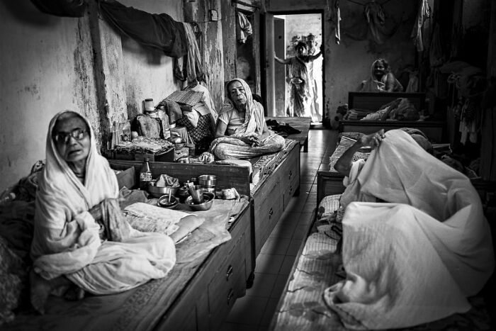 Black and white photo capturing a poignant moment in a modest room, featured in Budapest International Photo Awards.