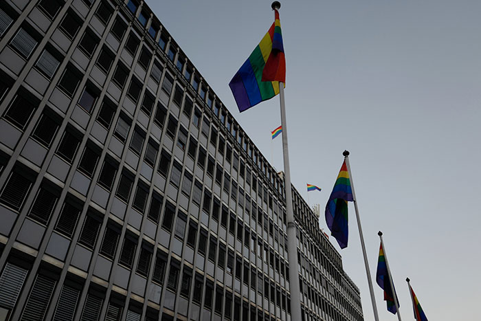 Modern office building with rainbow flags flying on poles against a clear sky, symbolizing community and acceptance.