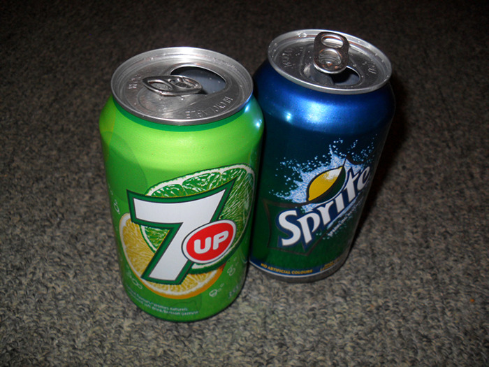Two soda cans, 7UP and Sprite, placed on a carpeted surface illustrating popular beverage branding conspiracies proven real.