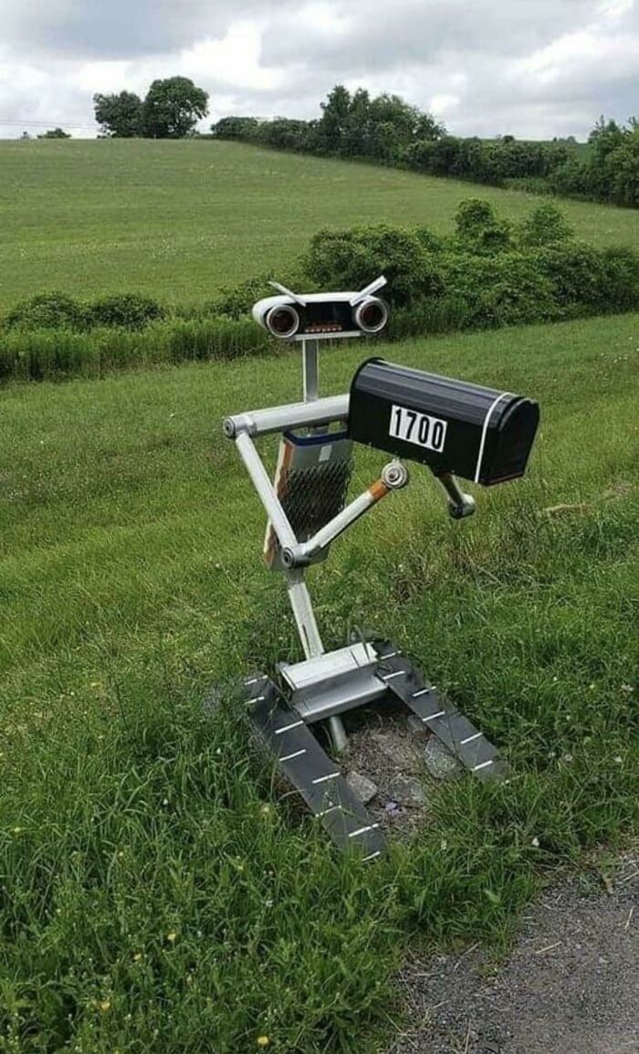 Creative and cool mailbox designed as a robot holding a black mailbox with number 1700 in a green field.