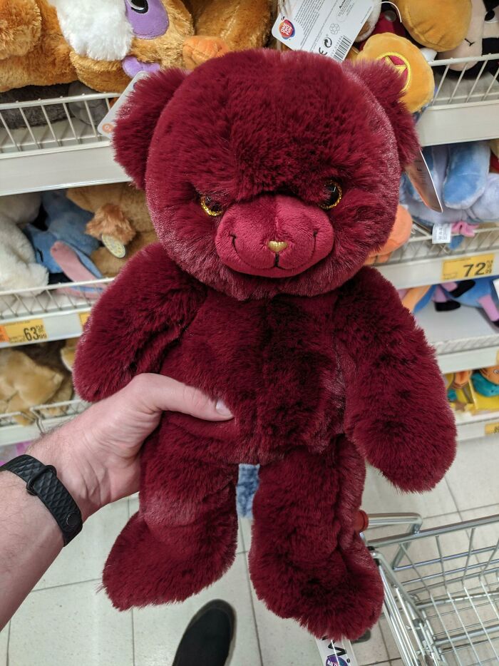 Hand holding a creepy plush toy bear with intense eyes in a store aisle of unsettling toys causing nightmares.