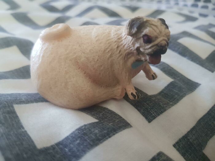 Creepy toy figurine of a pug dog with an unusual round body shape on patterned fabric background.
