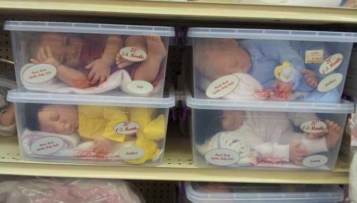 Four eerily lifelike creepy toys resembling babies stored in clear plastic boxes on a shelf in a store.