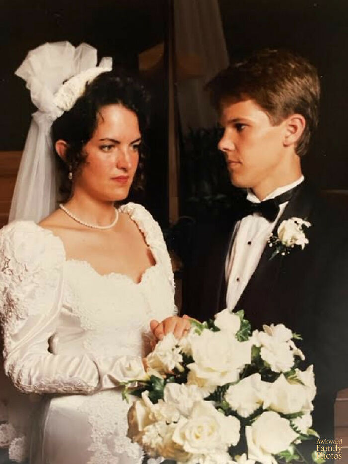 Awkward couple posing in wedding attire, bride holding bouquet, both looking serious.