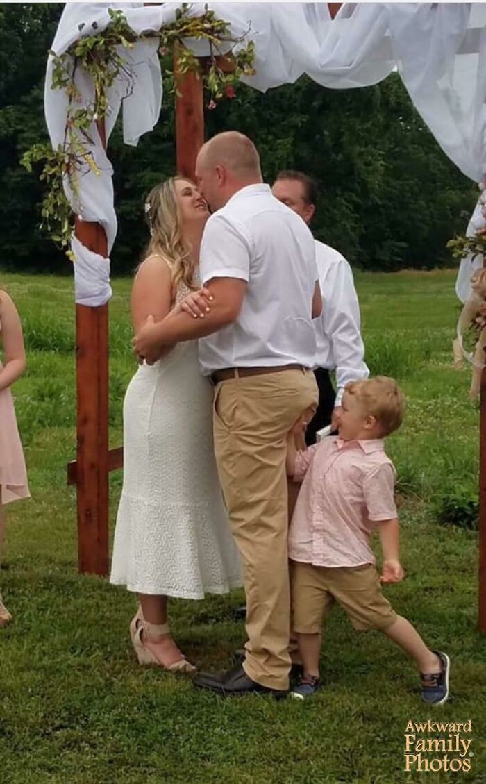 Funny couple photo with a child playfully grabbing the groom's pants during a wedding ceremony.