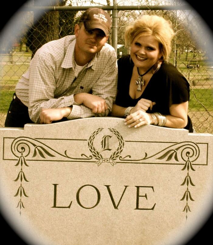 Couple posing humorously beside a large stone etched with "LOVE" in a park setting.