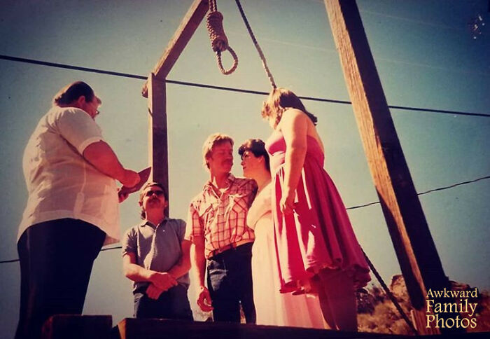 Funny couples' picture at a wooden gallows during a whimsical outdoor ceremony, capturing a humorous moment.