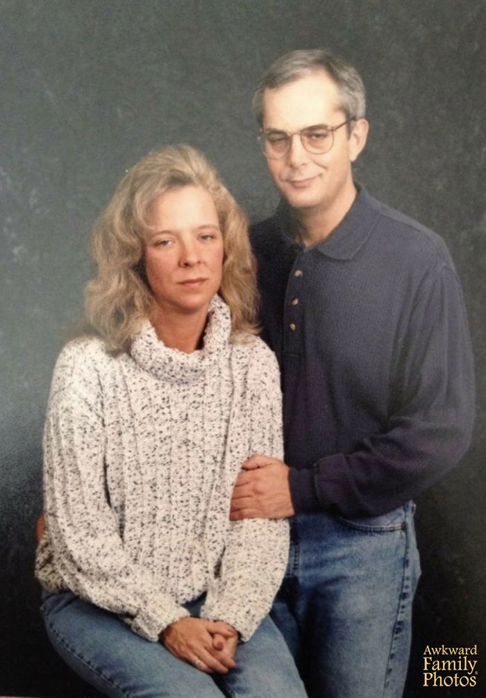 Awkward couples' portrait with serious expressions, wearing casual sweaters and jeans against a dark background.