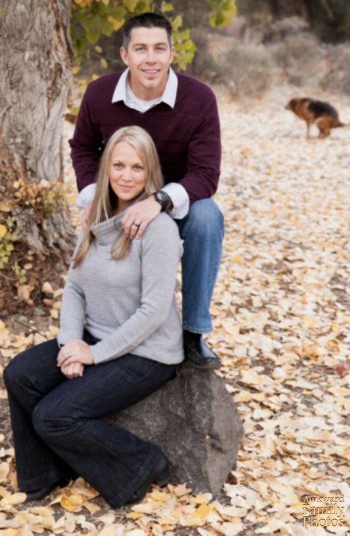 Couple posing outdoors on leaves, with a dog in the background; funny couples' picture.