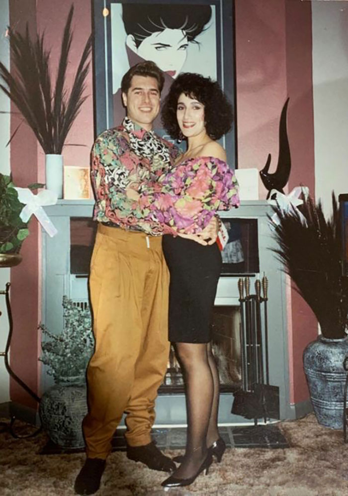 Couple posing in colorful outfits with a retro vibe, standing in a living room, showcasing a funny moment.