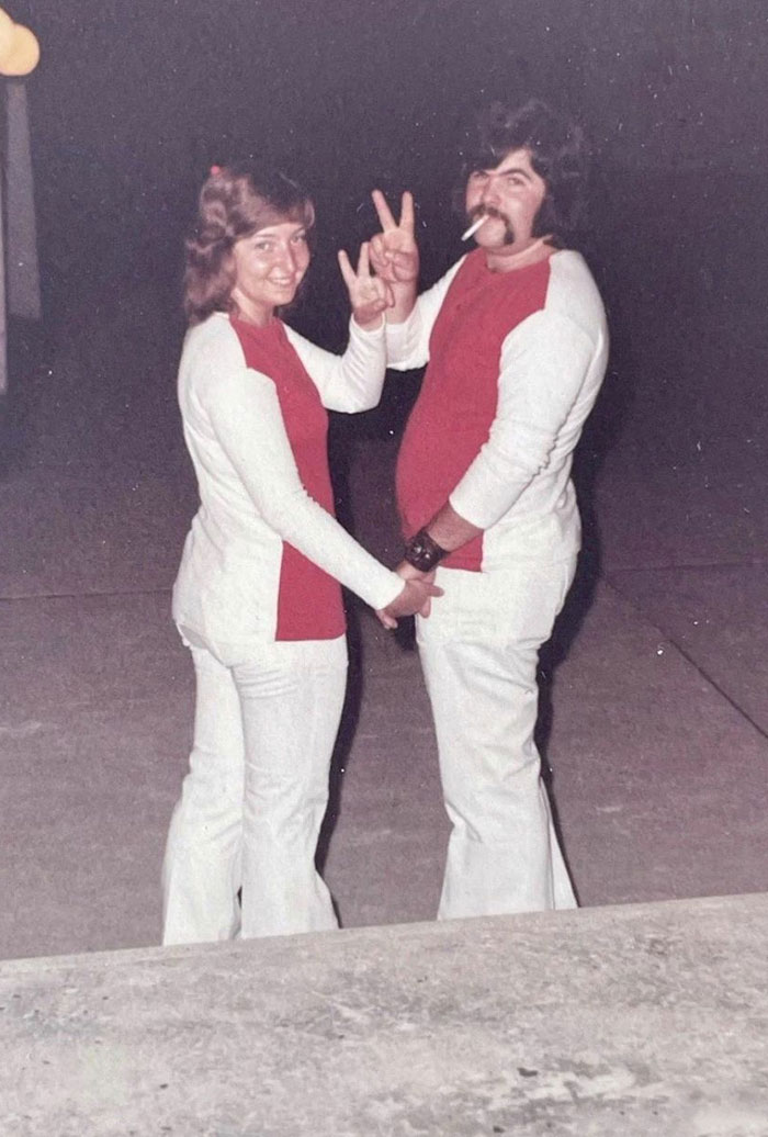 Couple in matching outfits, playfully posing while holding hands, with one person flashing a peace sign.