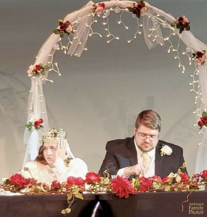 Funny couples' picture of a bride looking bored and a groom focused, under a floral arch at their wedding table.