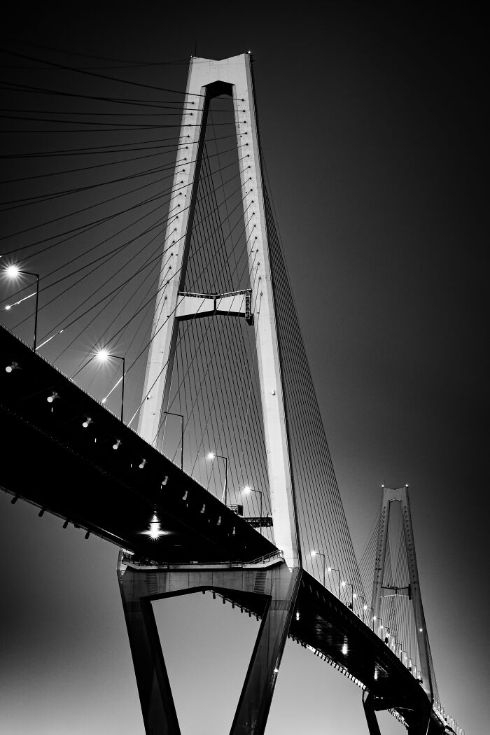 Black and white photo of a modern suspension bridge with dramatic lighting, featured in Budapest International Photo Awards.