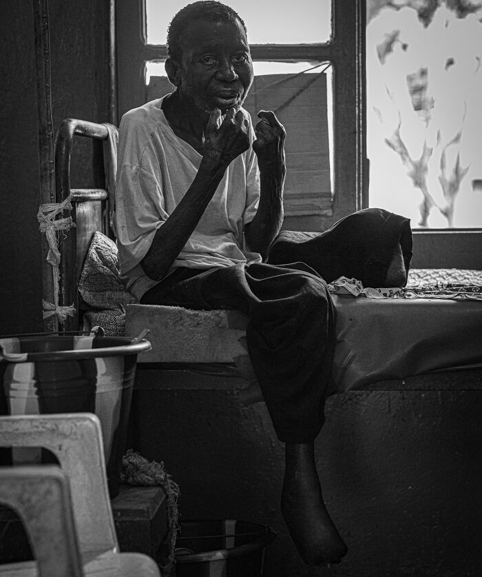 Elderly man sitting on a bed, captured in a powerful black and white portrait from Budapest International Photo Awards.
