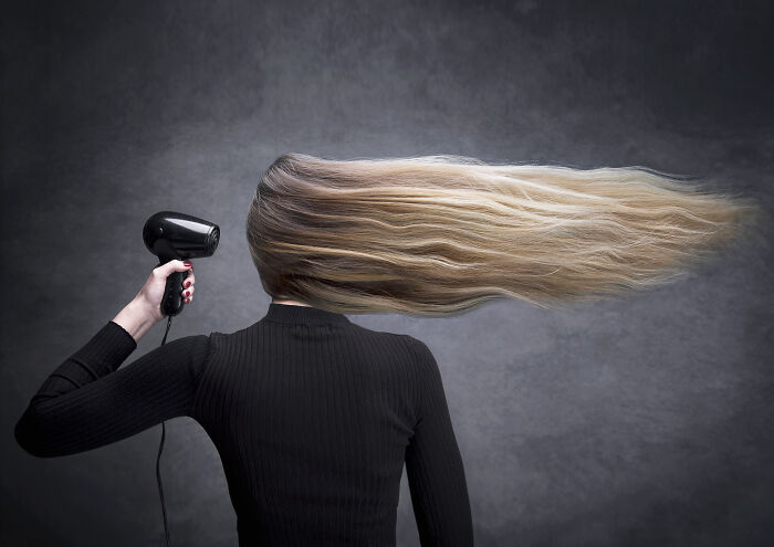Person with long blonde hair blown horizontally by a hairdryer, showcasing a creative shot from Budapest International Photo Awards winners.