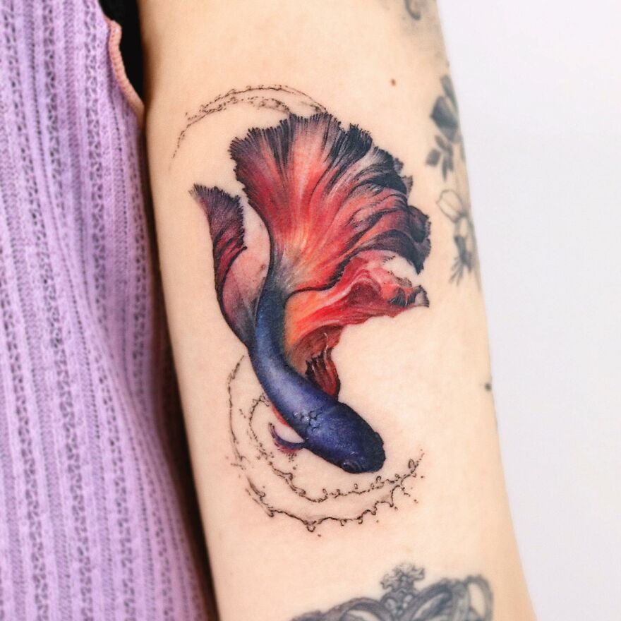 Colorful fish tattoo on arm, resembling a painting, with vivid red and blue hues.