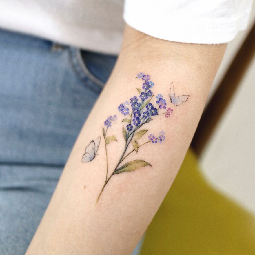 Arm with a painting-like tattoo of purple flowers and butterflies.