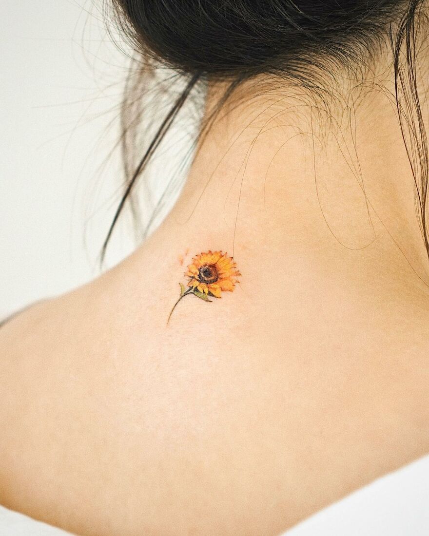 A small painting-like sunflower tattoo on the back of a woman's neck.