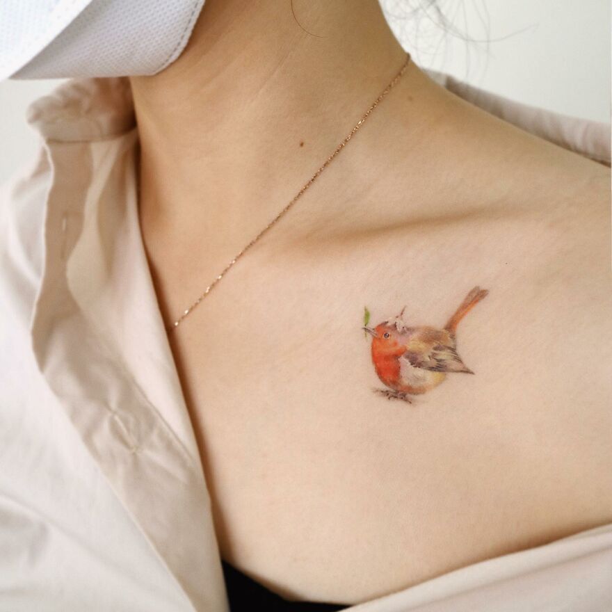 Delicate painting-like tattoo of a small bird on a person's collarbone.