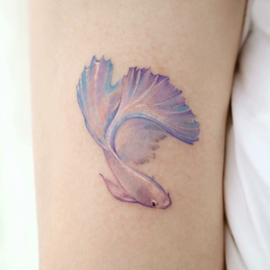 Painting-like tattoo of a pastel-colored fish on skin, showcasing intricate details and artistry.