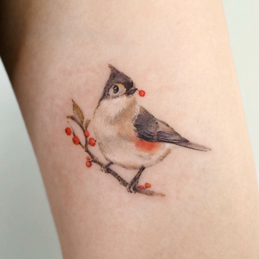 Painting-like tattoo of a bird perched on a branch with red berries.