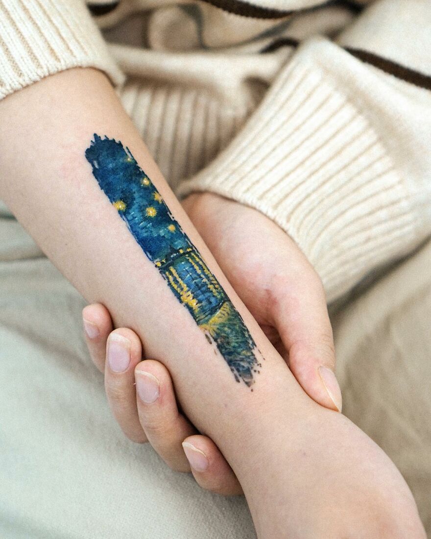 A painting-like tattoo on an arm, depicting a night sky with stars and water reflections.