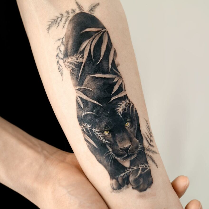 Painting-like tattoo of a panther on an arm, featuring detailed shading and foliage elements.