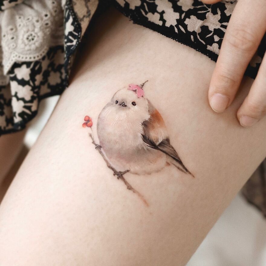 Painting-like tattoo of a bird with pink accents on a leg, showcasing intricate artistry.