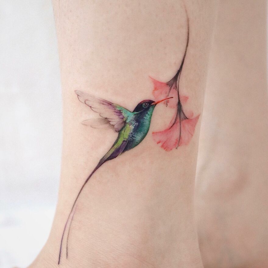 Painting-like tattoo of a colorful hummingbird with a flower on skin.